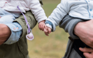 Zwei kleine Kinder werden im Arm gehalten und halten ihre gegenseitigen Hände.