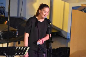 Eine schwarz gekleidete Frau singt in ein Mikrofon.