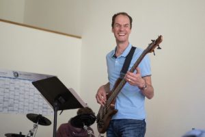 Mann spielt Bass-Gitarre und lacht.