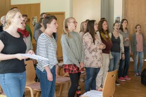 Eine Menschenmenge steht zwischen Stühlen und singt.