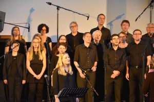 Singende Gruppe von schwarz gekleideten Menschen, eine blonde Frau singt ein Solo.