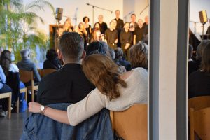 Zwei Menschen im Publikum schauen auf einen singenden Gospelchor im Hintergrund. Dabei hat die Frau ihren Kopf auf ihren Nachbarn gelegt und den Arm um ihn gelegt.